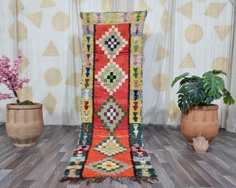 May include: A vibrant, rectangular runner rug with a central red field and geometric diamond patterns in various colors. The rug features a mix of yellow, green, blue, and orange accents. The rug is approximately 8 feet long.