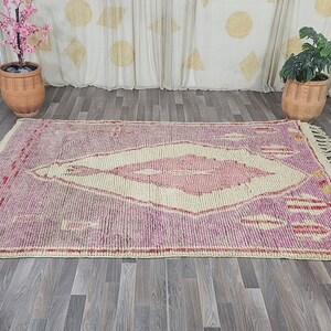 May include: A pink and cream Moroccan rug with a diamond-shaped pattern and fringe on the edges.