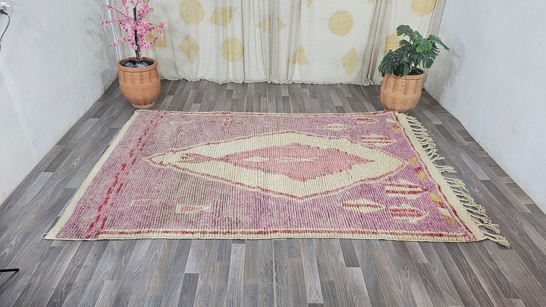 May include: A pink and cream Moroccan rug with a diamond-shaped pattern and fringe on the edges.