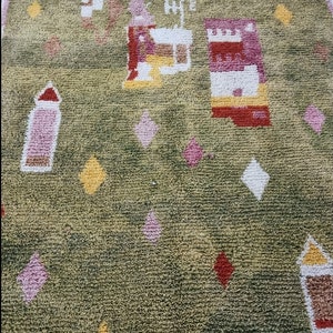 K&ouml;nnte beinhalten: Ein gr&uuml;ner Teppich mit einem geometrischen Muster in Rosa, Gelb, Wei&szlig; und Rot. Der Teppich hat einen Fransenrand.