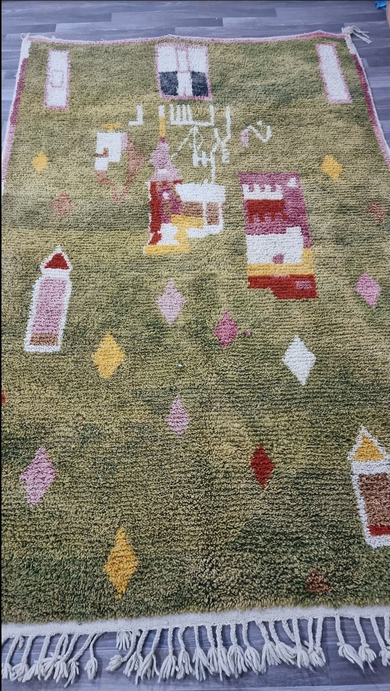 K&ouml;nnte beinhalten: Ein gr&uuml;ner Teppich mit einem geometrischen Muster in Rosa, Gelb, Wei&szlig; und Rot. Der Teppich hat einen Fransenrand.