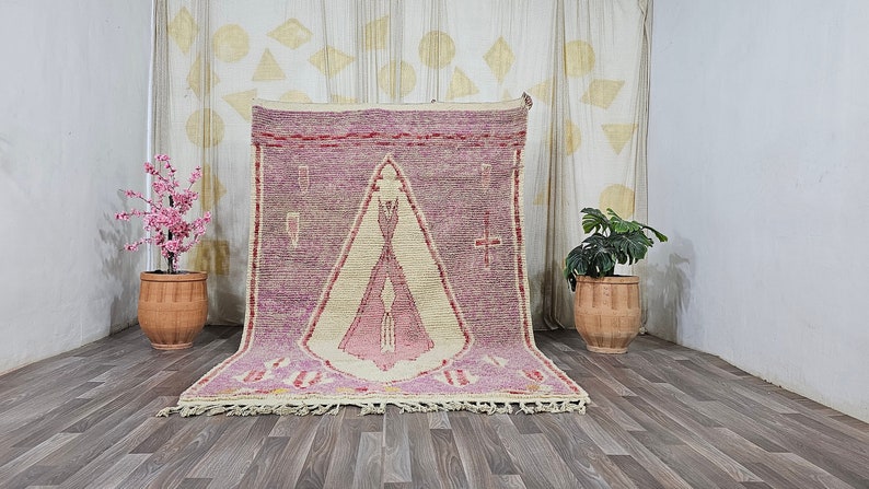 May include: A pink and cream Moroccan rug with a geometric pattern. The rug has a fringe border and is displayed on a wooden floor.