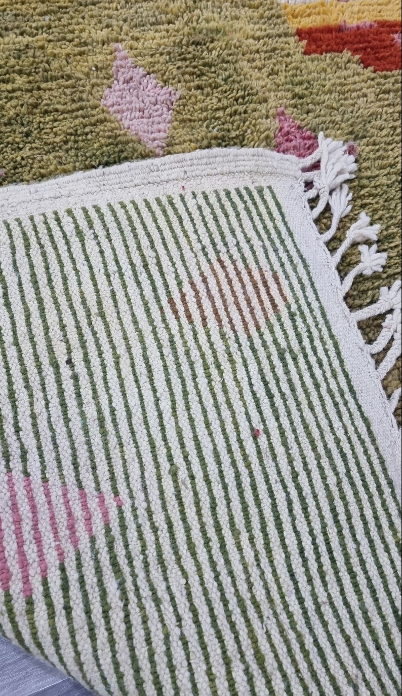 K&ouml;nnte beinhalten: Nahaufnahme eines wei&szlig;en und gr&uuml;nen gestreiften Teppichs mit Fransenrand. Der Teppich hat ein geometrisches Muster in Rosa und Braun.