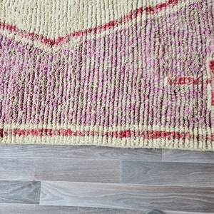 May include: Close-up of a pink and cream colored rug with a red geometric design. The rug has a soft, fuzzy texture.