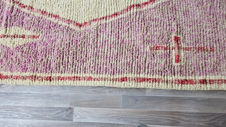 May include: Close-up of a pink and cream colored rug with a red geometric design. The rug has a soft, fuzzy texture.