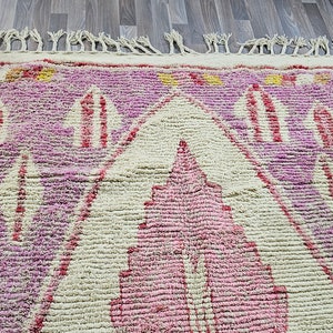 May include: A pink and cream Moroccan rug with a geometric pattern. The rug has a fringe border and is made of wool.