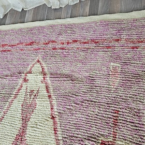 May include: A pink and white Moroccan rug with a geometric pattern. The rug has a fringe border and is made of wool.