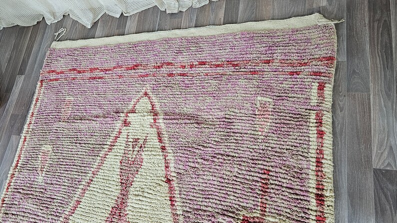 May include: A pink and white Moroccan rug with a geometric pattern. The rug has a fringe border and is made of wool.