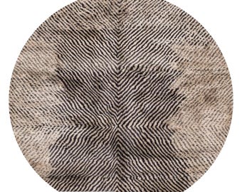 May include: Round rug with a geometric pattern. The rug features a central design of black and white chevron stripes radiating outwards. The outer edges have a lighter, beige tone, creating a contrast with the darker center. The rug is suitable for living rooms and bedrooms.