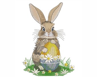 May include: A brown bunny rabbit holding a yellow and blue Easter egg decorated with white flowers. The bunny is sitting in a patch of green grass with white flowers.