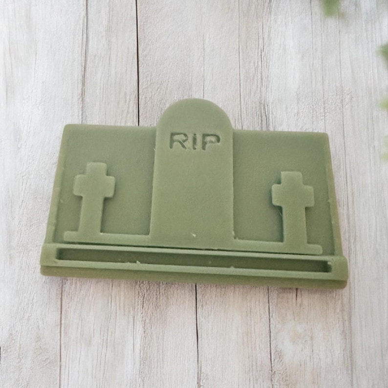 Puede incluir: Un objeto verde rectangular con forma de l&aacute;pida con las letras "RIP" talladas en la parte superior. Dos cruces est&aacute;n a cada lado de la l&aacute;pida. El objeto es probablemente un art&iacute;culo decorativo o un molde para manualidades.