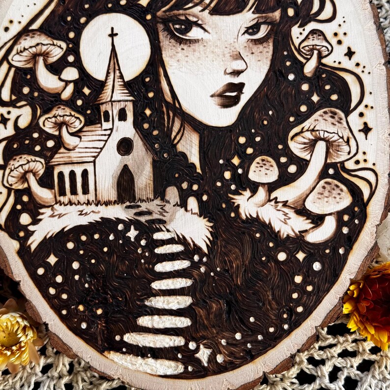 Pu&ograve; includere: Una fetta di legno circolare con un'illustrazione pirografata di una persona con lunghi capelli scuri, un edificio ecclesiastico, una luna piena e diversi funghi. L'opera utilizza ombreggiature in bianco e nero ad alto contrasto.