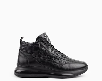 Puede incluir: Una zapatilla alta de color negro con textura acolchada en la parte superior, cordones negros y una suela gruesa totalmente negra. La lengüeta muestra un pequeño parche rectangular con texto blanco y una etiqueta de marca lateral.