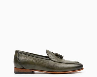 May include: An olive green leather loafer featuring a textured crocodile-embossed vamp, a decorative tassel detail on the front, a low stacked heel, and a smooth leather finish on the sides, presented against a plain white background.
