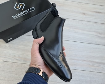 Puede incluir: Botas Chelsea de cuero negro con diseño de brogue y paneles laterales elásticos. Las botas tienen una punta puntiaguda y un tacón bajo.