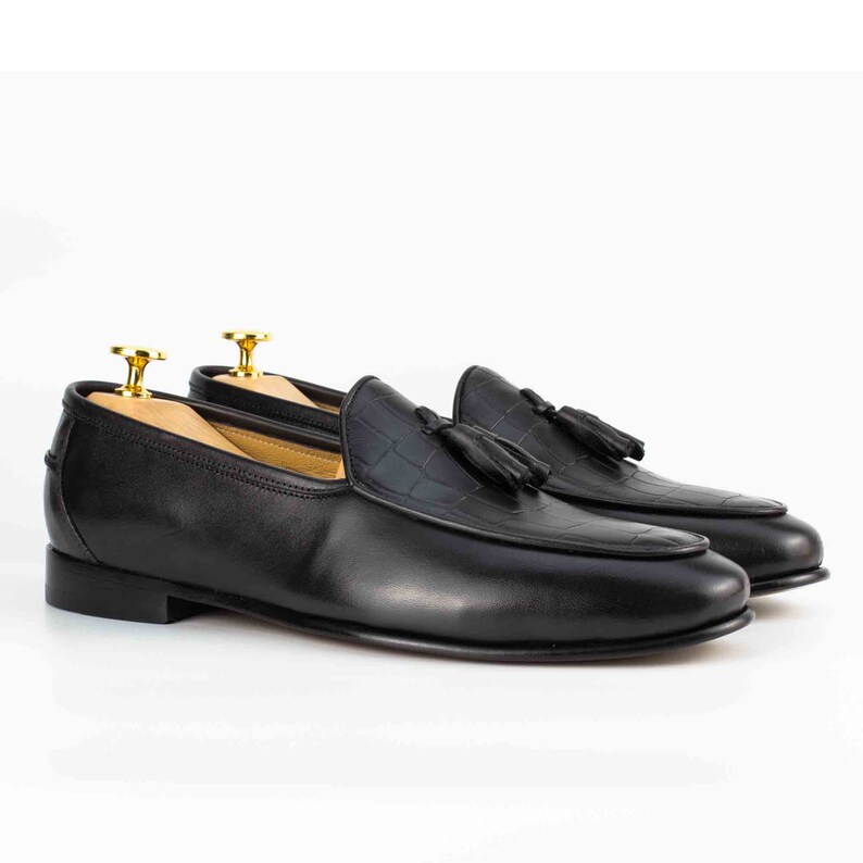 May include: Black leather tassel loafers with a crocodile-embossed pattern on the toe.