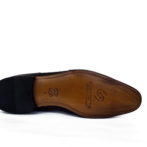 May include: The bottom of a brown leather dress shoe with a black rubber sole. The sole is stamped with the brand name "Scarpetta" and the words "Genuine Leather Made in Italy".