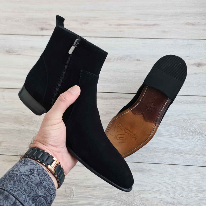 Puede incluir: Botas de tobillo de ante negro con cremallera lateral y suela de cuero marr&oacute;n. La suela tiene el texto "SCANDINAVIA" impreso.