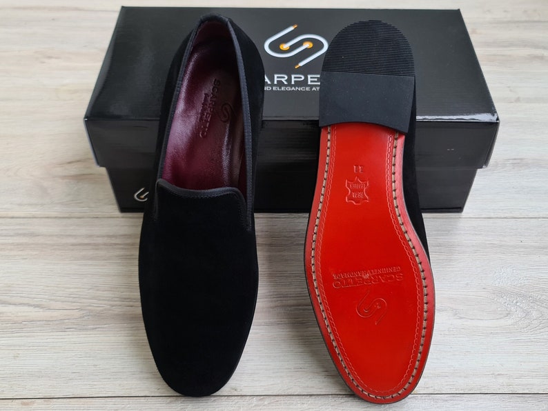 May include: A pair of black velvet slippers with a red leather sole. The sole has the brand name "SCARPE" printed on it.