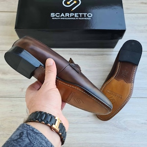 May include: A pair of brown leather loafers with a black sole. The loafers have a leather lining and a leather insole. The loafers are made by Scarpetto, a brand that emphasizes quality and elegance.