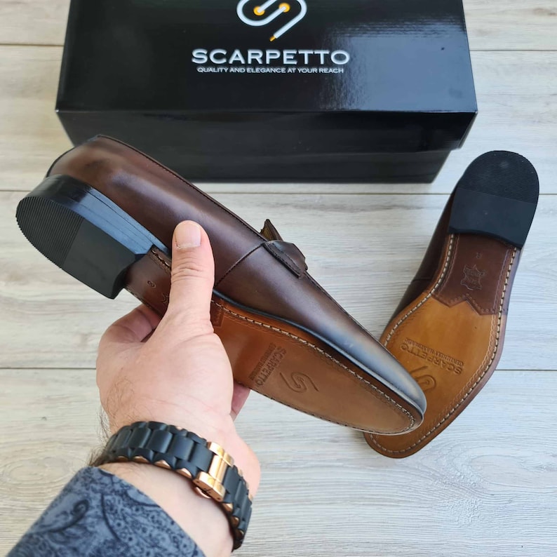 May include: A pair of brown leather loafers with a black sole. The loafers have a leather lining and a leather insole. The loafers are made by Scarpetto, a brand that emphasizes quality and elegance.