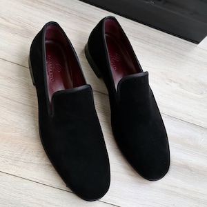 May include: A pair of black velvet loafers with a red leather lining. The loafers have a pointed toe and a slip-on design.