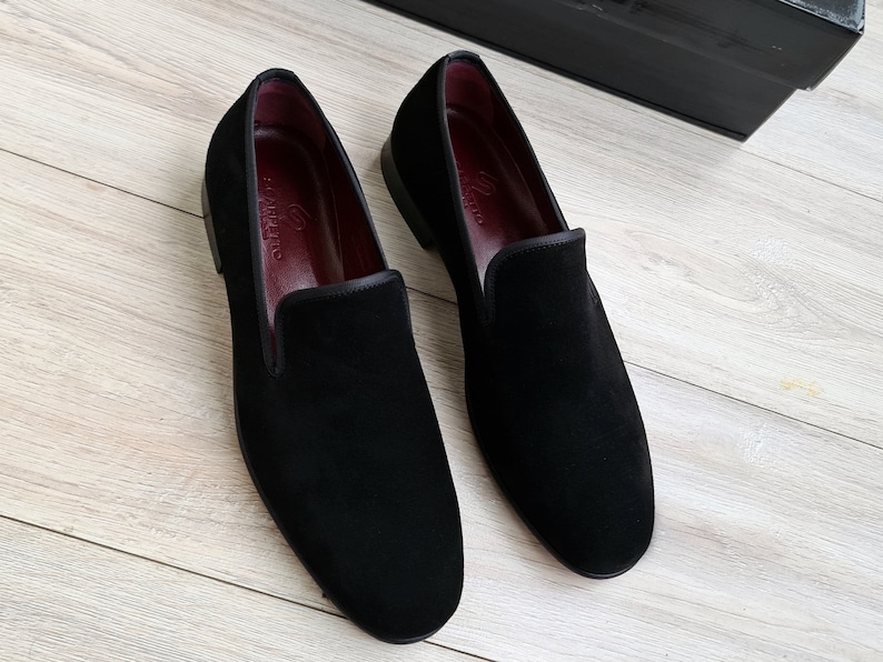 May include: A pair of black velvet loafers with a red leather lining. The loafers have a pointed toe and a slip-on design.