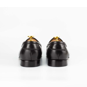May include: A pair of black leather loafers with a gold accent on the back. The loafers are on a white background.