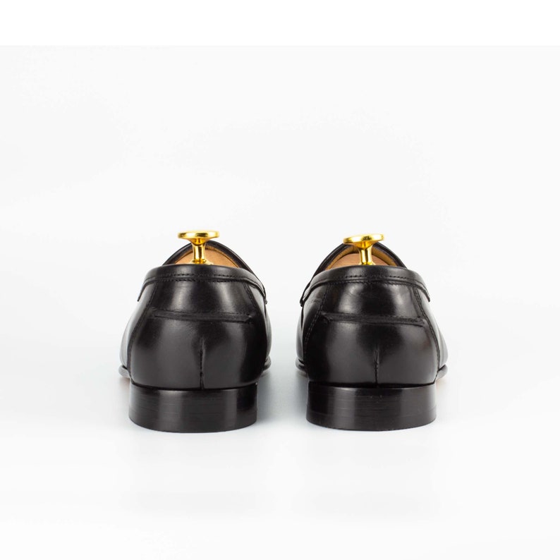 May include: A pair of black leather loafers with a gold accent on the back. The loafers are on a white background.
