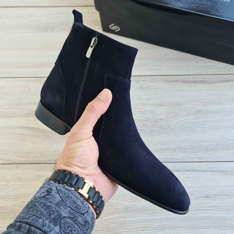 Puede incluir: Un par de botines de ante azul oscuro con cremallera en la parte posterior. Los botines tienen una punta puntiaguda y un tac&oacute;n bajo.
