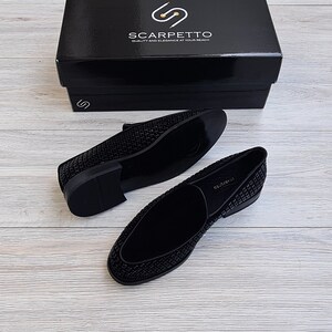 May include: A pair of black velvet loafers with a sparkly, textured design. The loafers are on a light wood surface.