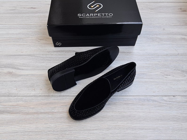 May include: A pair of black velvet loafers with a sparkly, textured design. The loafers are on a light wood surface.