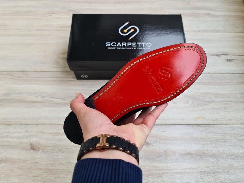 May include: A close-up of the red leather sole of a black shoe. The sole has a stitched edge and the brand name "Scarpetto" is embossed in the leather.