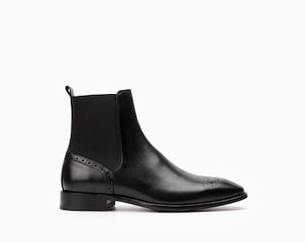 Può includere: Uno stivaletto Chelsea in pelle nera con punta affusolata e perforazioni decorative brogue, un dettaglio brogue abbinato sul tallone, inserti laterali elastici e un piccolo tacco con una linguetta sulla parte superiore della caviglia.