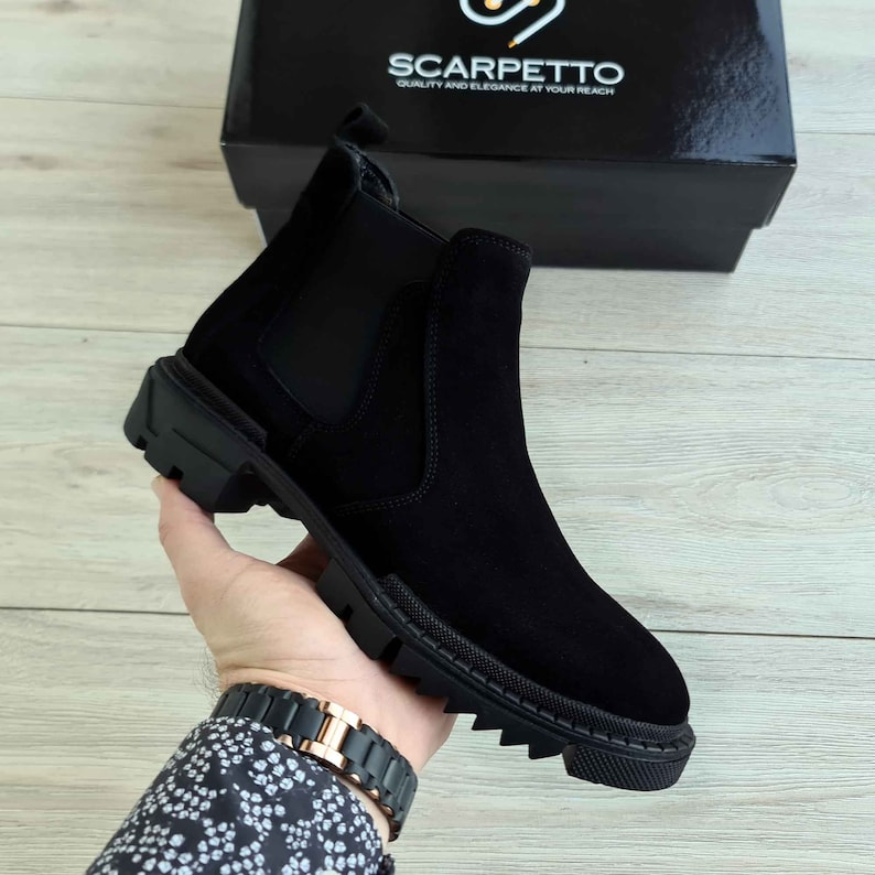 Peut inclure: Bottines Chelsea en daim noir avec une &eacute;paisse semelle en caoutchouc et une languette de traction. Les bottes ont une semelle textur&eacute;e et un d&eacute;tail cousu autour du haut.