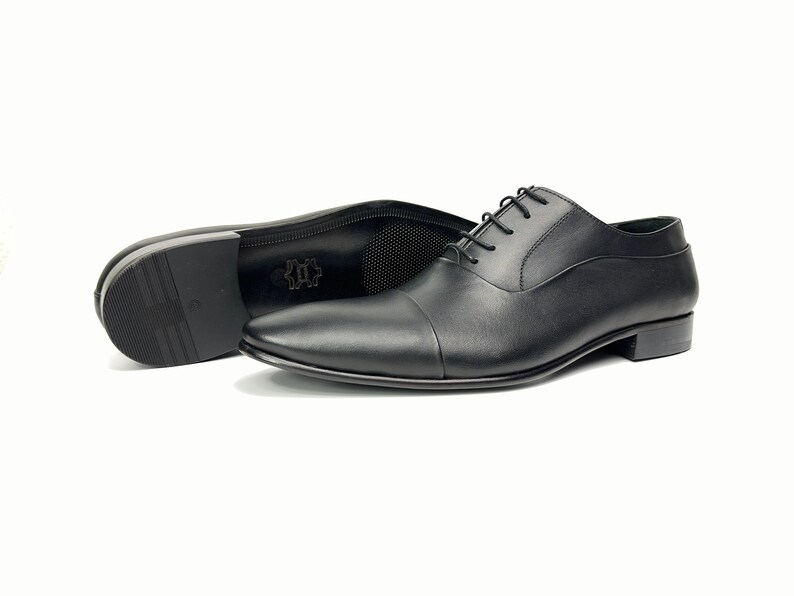 May include: A pair of black leather lace-up shoes with a cap toe design. The shoes are on a white background.
