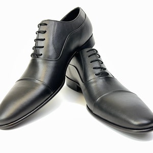 May include: A pair of black leather lace-up shoes with a cap toe design.
