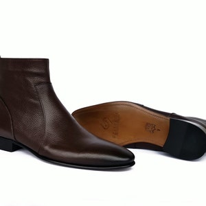 May include: Brown leather ankle boots with a pointed toe and a zipper on the side. The boots have a low heel and a rubber sole.