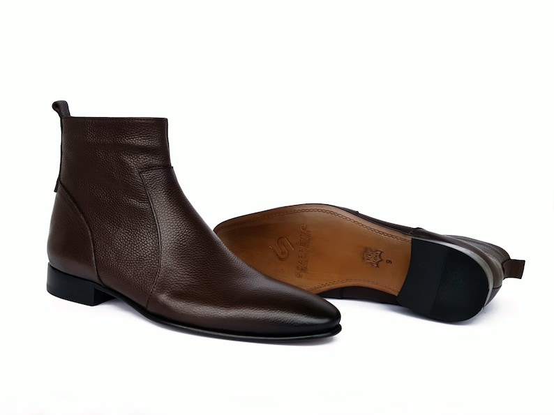 May include: Brown leather ankle boots with a pointed toe and a zipper on the side. The boots have a low heel and a rubber sole.