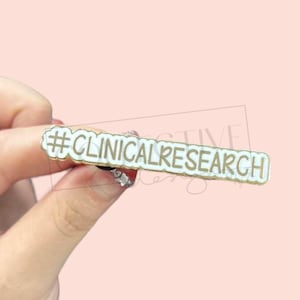 May include: Gold and white enamel pin with the text "#CLINICALRESEARCH" in gold lettering.
