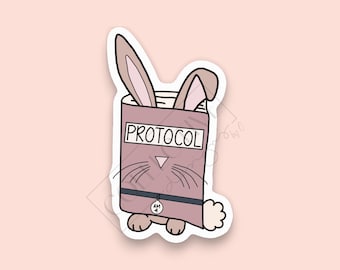 Può includere: Un libro rosa con la parola "PROTOCOL" sulla copertina. Un coniglio dei cartoni animati spunta dal libro con le orecchie che sporgono. Il coniglio indossa un collare nero con un'etichetta che dice "AM 4".