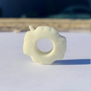 May include: A white plastic ring with a textured surface and a small hole in the center.
