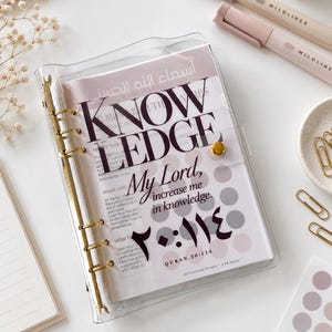 May include: A clear plastic six-ring binder featuring a cover insert with the text KNOWLEDGE My Lord, increase me in knowledge. Quran 20:114, alongside Arabic script. The binder has gold-toned metal rings and a gold-toned snap closure button.