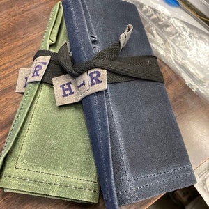 May include: Two fabric rolls, one green and one blue, are tied together with a black ribbon. The ribbon has a label that reads "H-R".
