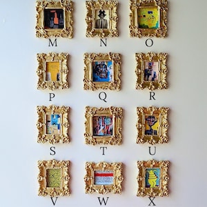 May include: A collection of twelve framed artworks with gold ornate frames. The artworks feature various abstract and figurative paintings in vibrant colors. Each frame is labeled with a letter from M to X.