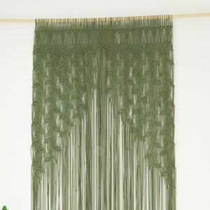 May include: A green macrame wall hanging with a leaf pattern. The hanging is made of cotton cord and is attached to a wooden dowel.