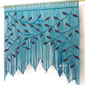 Pode incluir: Uma tapeçaria de parede de macramé turquesa com uma haste de madeira. O design apresenta padrões de folhas vermelhas em galhos. A borda inferior tem um design ondulado com pequenas contas de madeira. A tapeçaria de parede é exibida em uma parede branca.