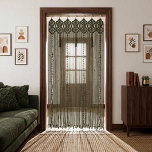Olive green macrame valance featuring intricate geometric diamond knotwork, three decorative tassels, and long vertical rope strands on a natural wooden rod.