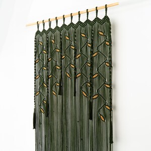 Close-up of a botanical fiber art tapestry with deep forest green vines and tan leaf details.