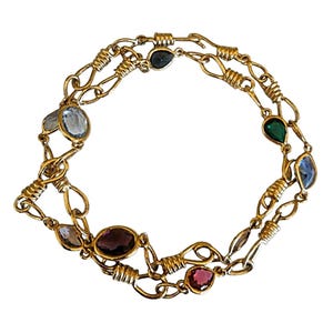 May include: A gold chain necklace with a variety of colorful gemstones, including clear, blue, green, purple, and pink.